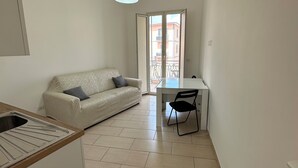 A small, modern apartment with a kitchenette, a sofa, a dining table with a chair, and a balcony with a view. - Room25 InCentro Guest House (Cercola)