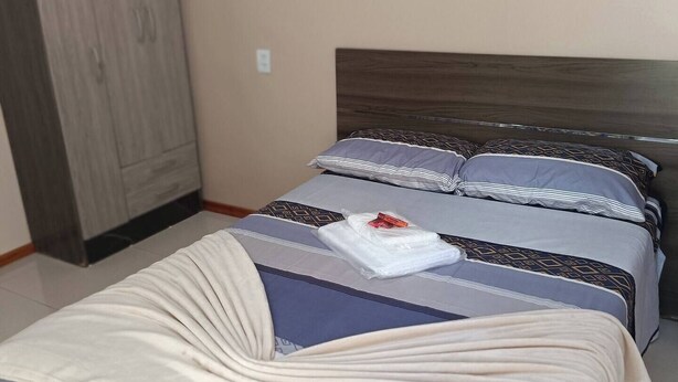 Una cama bien tendida con una colcha y almohadas a rayas, un cabecero de madera y un armario al fondo.