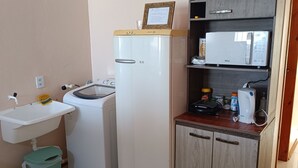 Cocina compacta con lavadora, pileta, microondas y un mueble pequeño.