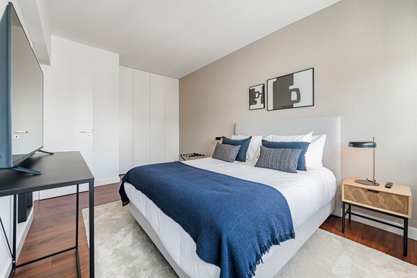 A modern bedroom with a bed, a desk, and a TV.