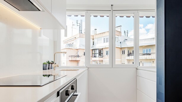 Una cocina moderna con armarios blancos, un lavamanos de acero inoxidable y una ventana con vistas a una zona residencial.