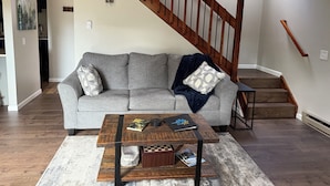 Ein Wohnzimmer mit grauem Sofa, einem Holztisch und einer Treppe mit Holzhandläufen.