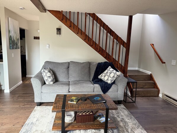 A living room with a gray sofa, a wooden coffee table, and a staircase with wooden railings.