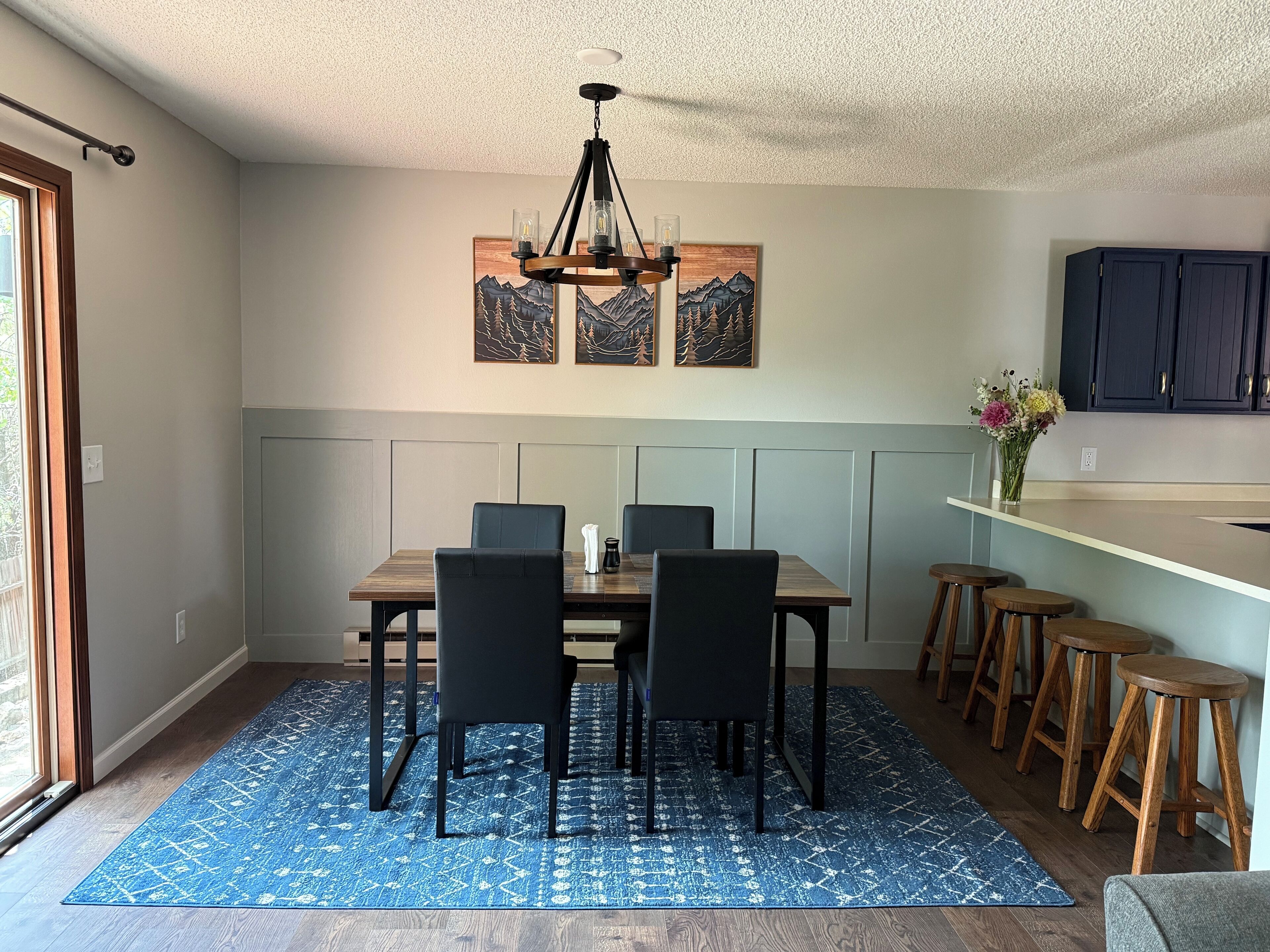 A dining area with a wooden table, black chairs, a blue patterned rug, and a chandelier.