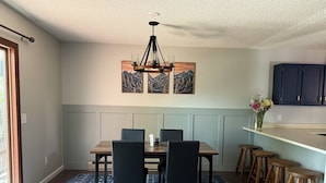 Ein Essbereich mit Holztisch, schwarzen Stühlen, einem blauen Teppich mit Muster und einer Chandelier.