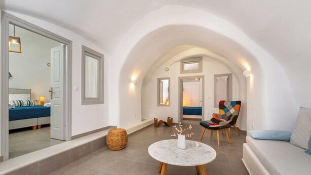 Un intérieur moderne avec un haut plafond en arc de cercle, une table ronde en marbre surmontée d’un vase blanc, une chaise colorée et un canapé agrémenté d’un coussin bleu.