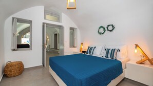 Une chambre à coucher avec un grand lit, deux tables de chevet, un luminaire suspendu et une porte donnant sur une autre pièce.