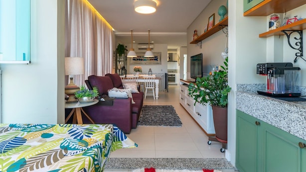 A cozy living room with a sofa, a dining table, and a kitchen area with a coffee machine. - Residencial Ilha de Navagio (Bombinhas)
