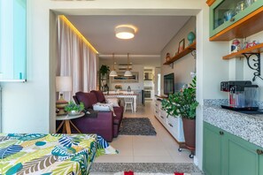A cozy living room with a sofa, a dining table, and a kitchen area with a coffee machine.