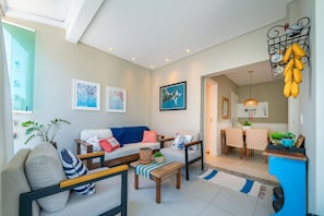 Een moderne woonkamer met een bank, salontafel en stoelen, een eethoek met een tafel en stoelen, en een keuken die zichtbaar is door een open doorgang.