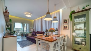 A dining area with a wooden table, white chairs, and hanging pendant lights. - Residencial Ilha de Navagio (Bombinhas)