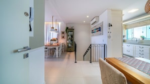 A modern kitchen with white cabinets, a wooden dining table, and a staircase leading to another level. - Residencial Ilha de Navagio (Bombinhas)