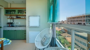 A modern kitchen with green cabinets, a built-in oven, and a window overlooking a construction site. - Residencial Ilha de Navagio (Bombinhas)