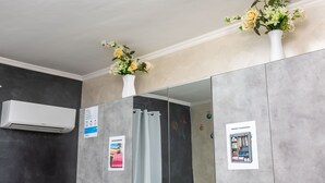 Un baño con pared de mármol gris, un aire acondicionado blanco, un espejo con un florero blanco y un cartel en la pared.