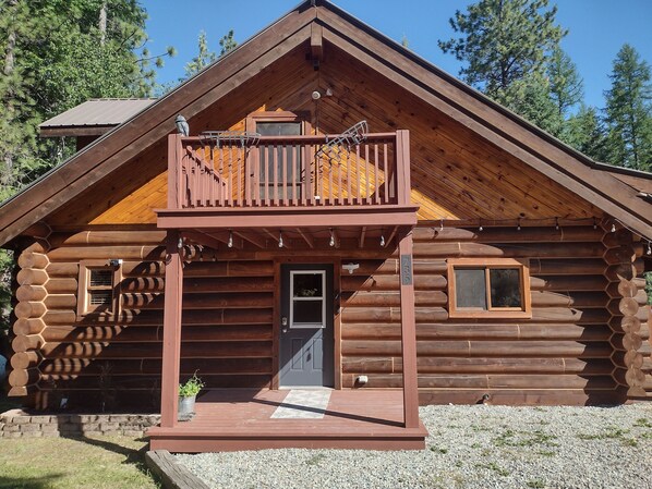 Una cabaña de madera con un balcón, una puerta principal y una ventana pequeña.