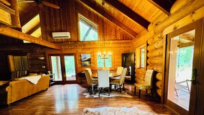 A log cabin interior with a dining area, wooden walls, and large windows.