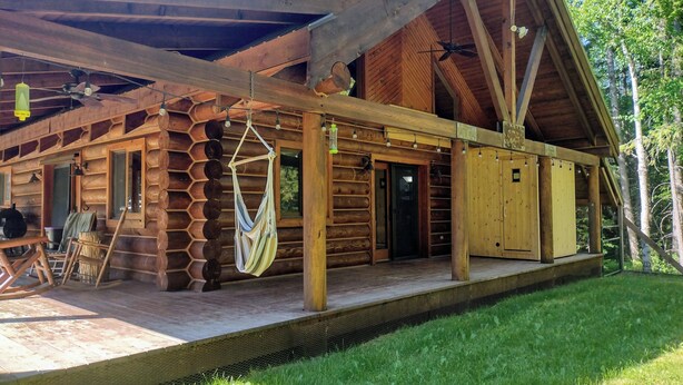 A log cabin with a porch, a hammock, and a wooden deck.