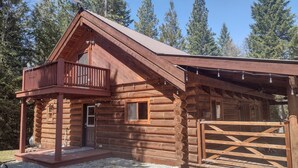A log cabin with a balcony, a covered porch, and a wooden gate.