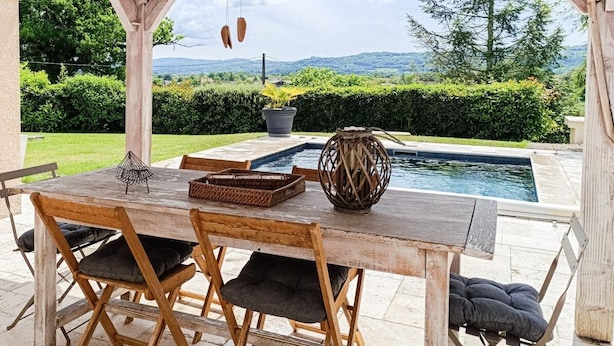 A wooden pergola with a pool table and chairs, overlooking a swimming pool and lush greenery. - Gîtes de France® - Lyna's Villa (PUYBRUN)