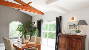A dining area with a wooden table, beige chairs, a potted plant, and a cabinet with decorative items. - Gîtes de France® - Lyna's Villa (PUYBRUN)