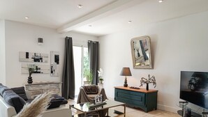 A modern living room with a sofa, a coffee table, a TV, and artwork on the walls. - Gîtes de France® - Lyna's Villa (PUYBRUN)