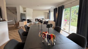 Ein modernes Wohnzimmer mit einem großen schwarzen Esstisch, einer farbenfrohen Elefantenskulptur und Blick ins Freie durch große Fenster.