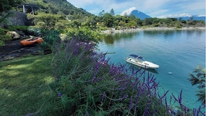 Un cadre paisible au bord d’un lac, avec un bateau amarré près du rivage, entouré d’une végétation luxuriante et avec une montagne en arrière-plan.
