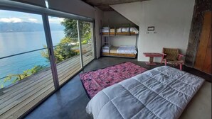 Une chambre avec une grande fenêtre donnant sur un lac, un lit superposé, une table de chevet et une chaise.