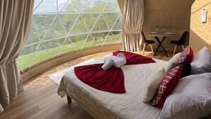 Ein gemütliches, kreisrundes Schlafzimmer im Zeltstil mit einem großen Bett, Vorhängen, einem kleinen Tisch und Blick ins Freie.