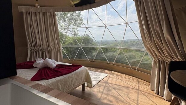 Ein Schlafzimmer mit einem großen Bett, einem Schreibtisch und Blick ins Freie durch ein großes Fenster.