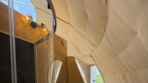 Ein kompakter, moderner Zeltraum mit Holzvertäfelung, integriertem Waschbecken und einer Duschkabine aus Glas.