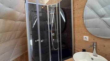 A compact, modern bathroom with a glass-enclosed shower, a round sink, and a wooden vanity.