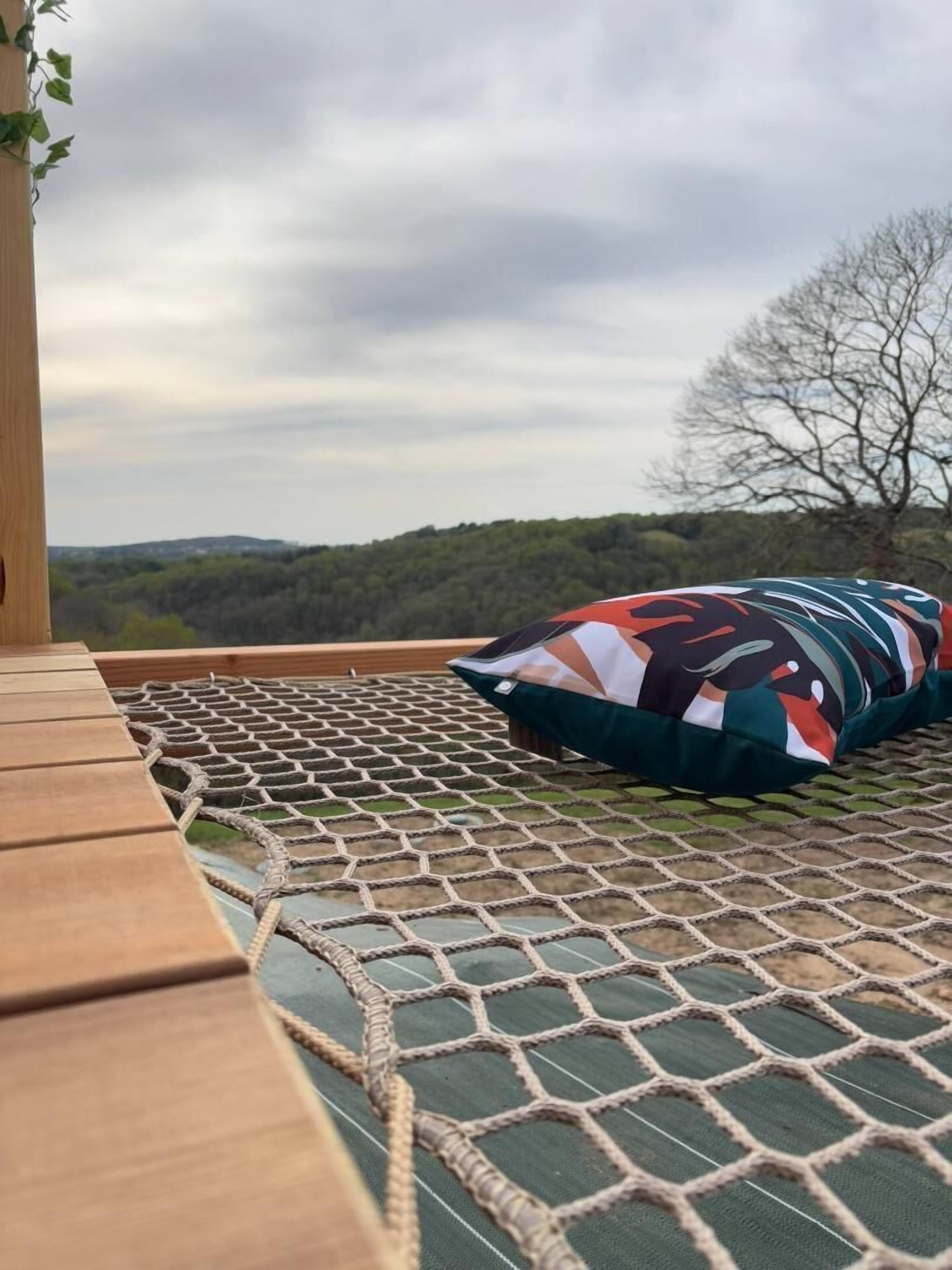 Un hamac sur une terrasse en bois, avec vue sur un paysage boisé.