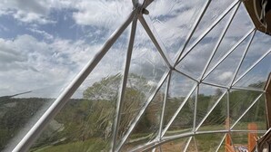 Eine geodätische Kuppel mit Blick auf eine hügelige Landschaft durch transparente Paneele.