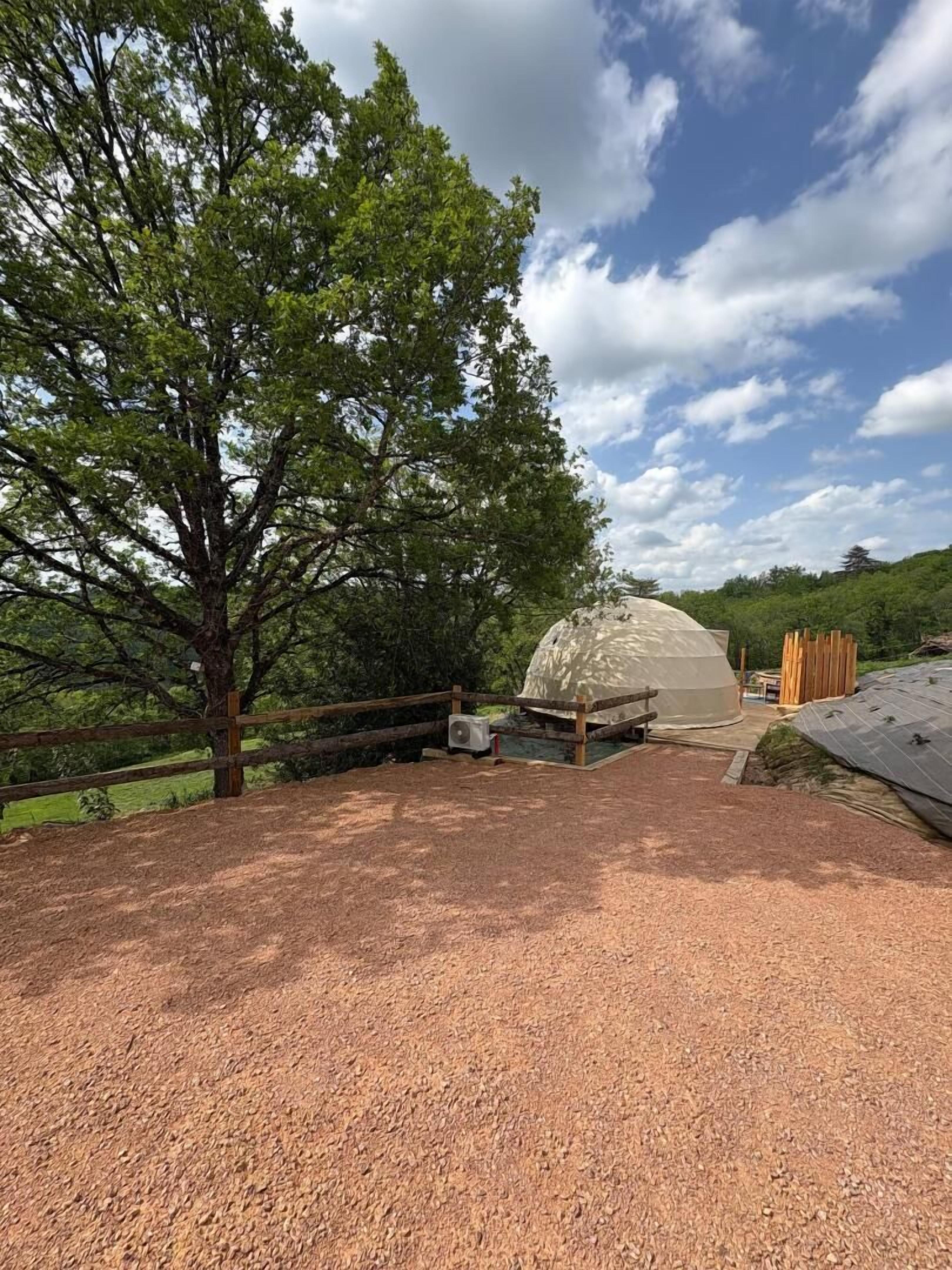 A dome-shaped structure with a gravel-covered ground, surrounded by a wooden fence and trees.