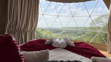Una camera da letto con un'ampia finestra, un letto con biancheria rossa e bianca e vista sul verde circostante.