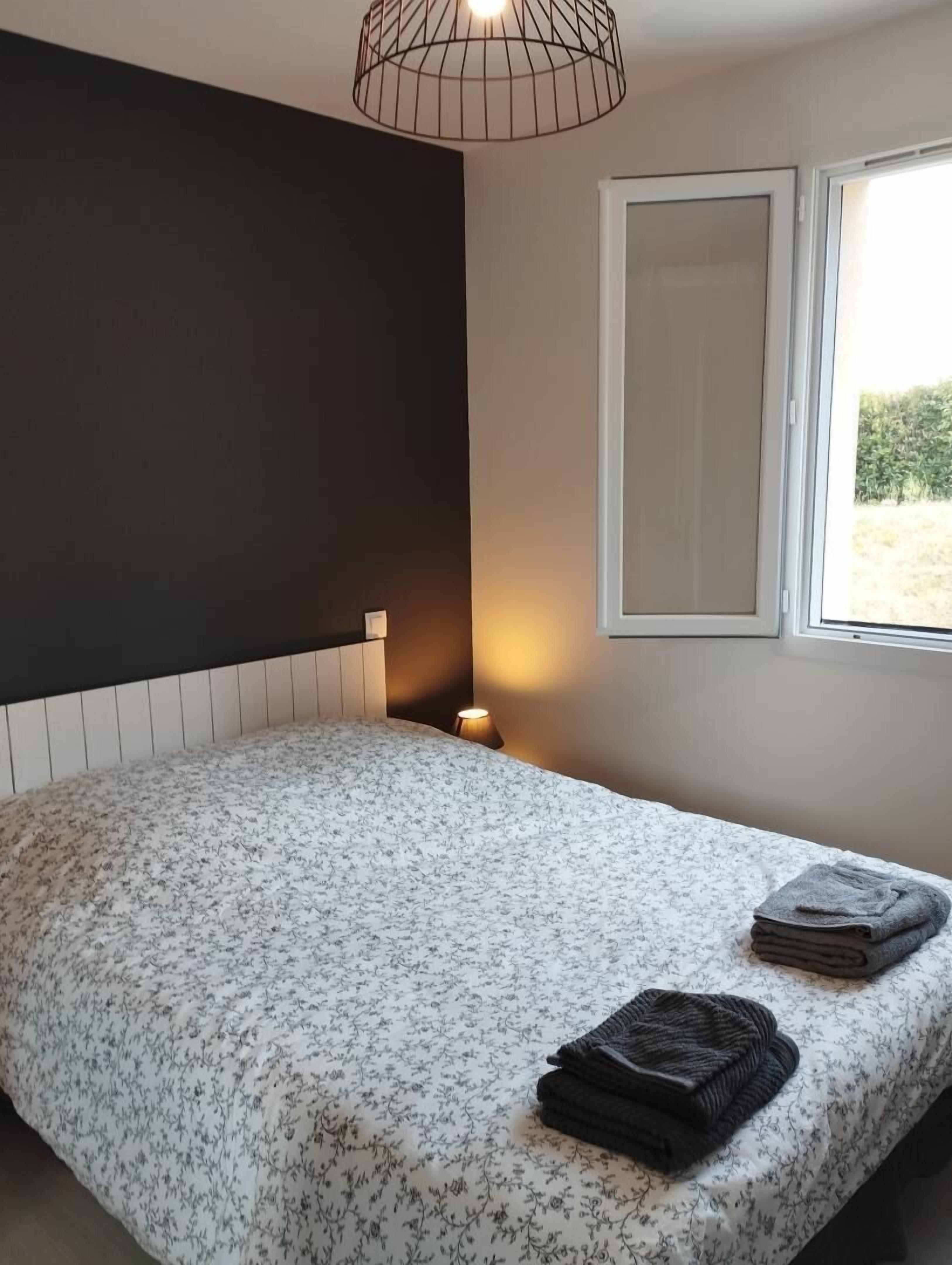 Un dormitorio con cama, una lámpara de noche, una ventana y vistas al verdor exterior.