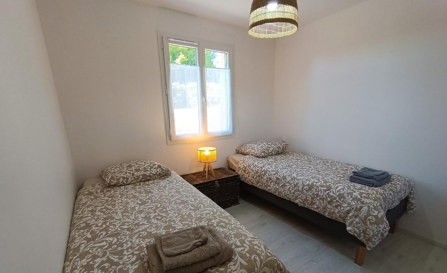 A small, well-lit bedroom with two beds, a window, and a bedside lamp.
