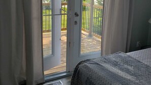 A bedroom with a bed, a sliding glass door leading to a deck, and a view of a green landscape. - Waterfront Family Oasis – Comfort & Charm (Amaranth)