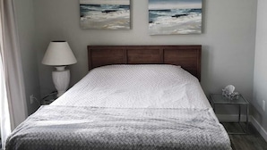 A bedroom with a bed, a nightstand, a lamp, two wall-mounted paintings, and a small table with a tissue box. - Waterfront Family Oasis – Comfort & Charm (Amaranth)