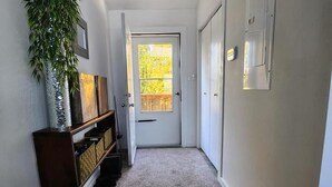 A hallway with a door, a potted plant, a wooden cabinet, and a carpeted floor. - Waterfront Family Oasis – Comfort & Charm (Amaranth)