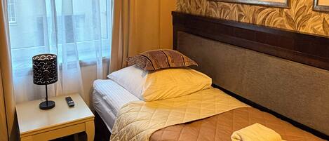 A hotel room with a bed, a nightstand with a lamp, a remote control, and a painting on the wall.
