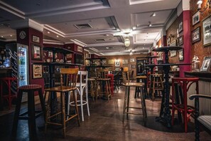 A bar area with multiple stools and tables, a refrigerator, and framed pictures on the walls. - Royal Rooms (Poznan)