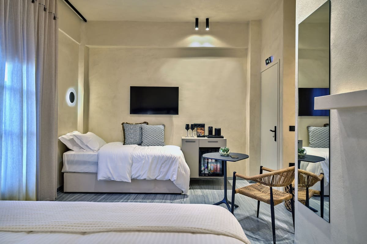 Une chambre d’hôtel moderne avec un grand lit, un petit bureau, une télévision et un fauteuil en osier.