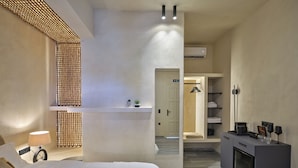 A modern hotel room with a large bed, a bedside table with a lamp, a wardrobe, and a seating area with a small table and chairs. - Anchorage Paros  (Piso Livadi)