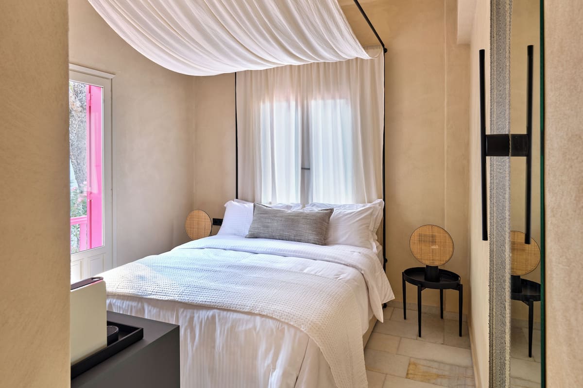 Une chambre à coucher avec un lit, des tables de chevet, un baldaquin et une fenêtre avec des rideaux.