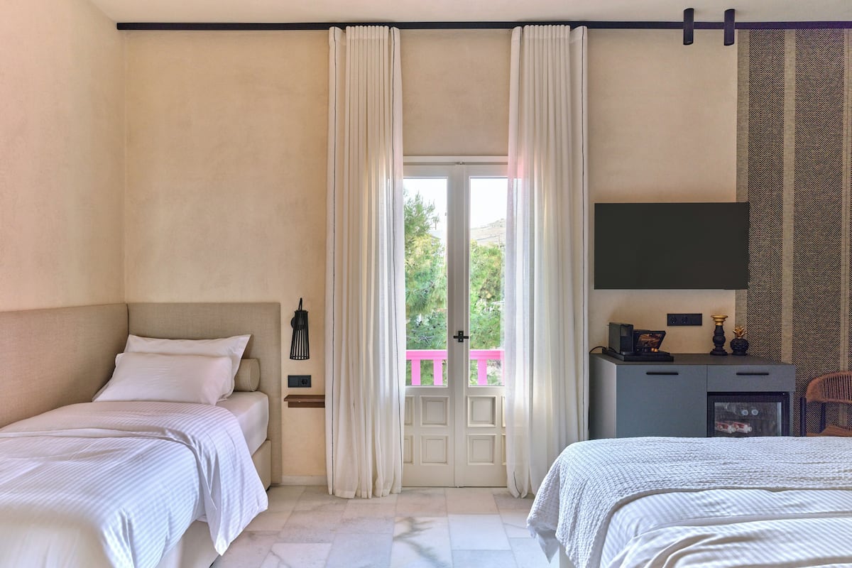 Une chambre d’hôtel avec deux lits, un téléviseur fixé au mur, un bureau avec une lampe et une vue sur la verdure à l’extérieur.