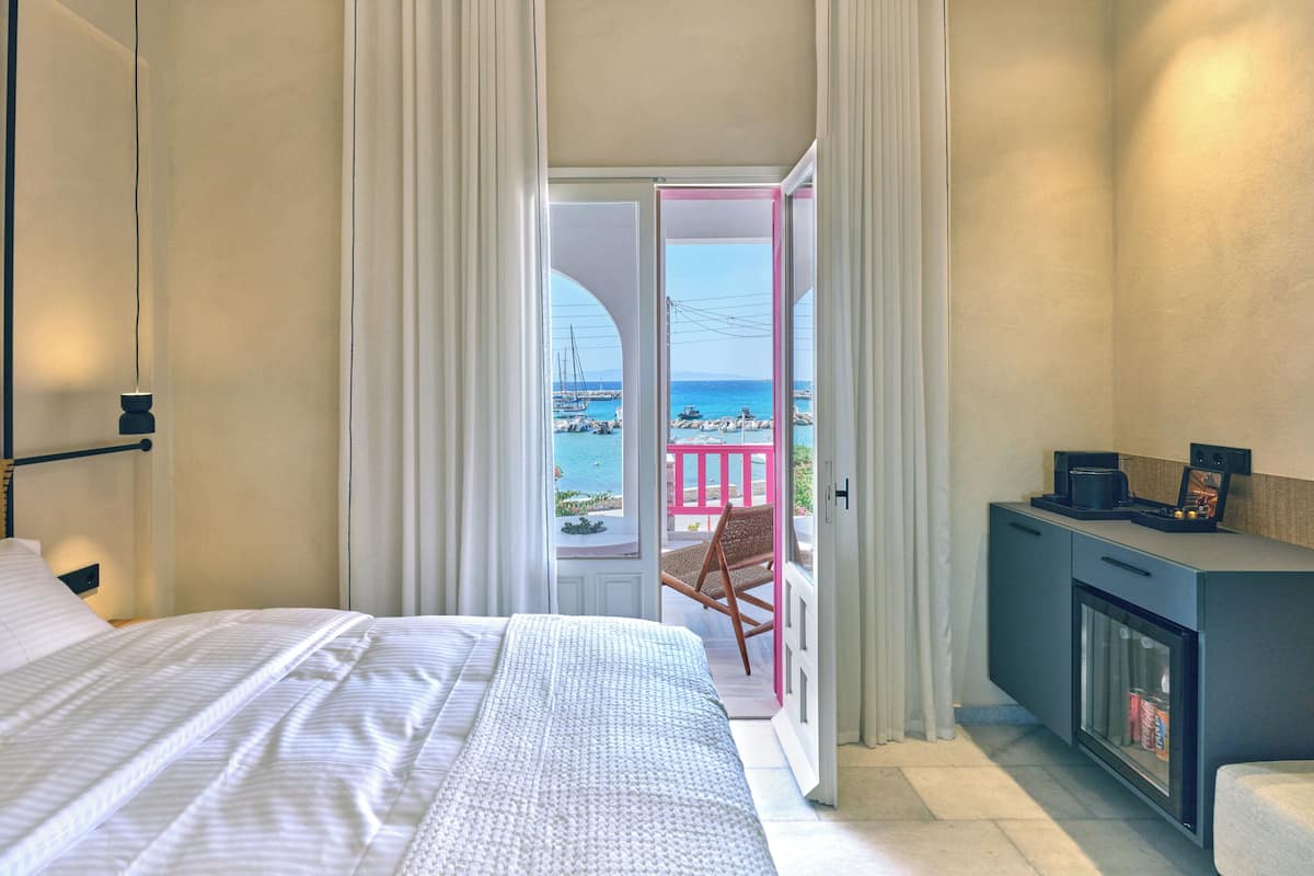Une chambre à coucher avec un lit, une chaise, un bureau et une vue sur la mer, visible par la porte.