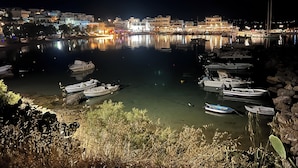 A nighttime marina with boats docked, calm water, and buildings with lights reflecting on the water. - Anchorage Paros  (Piso Livadi)