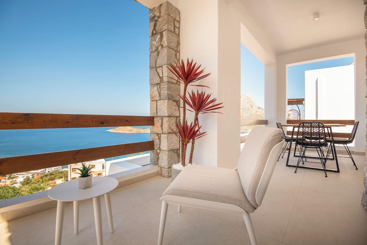 A balcony with a view of the sea, a stone pillar, a potted plant, a white chair, and a table with chairs.